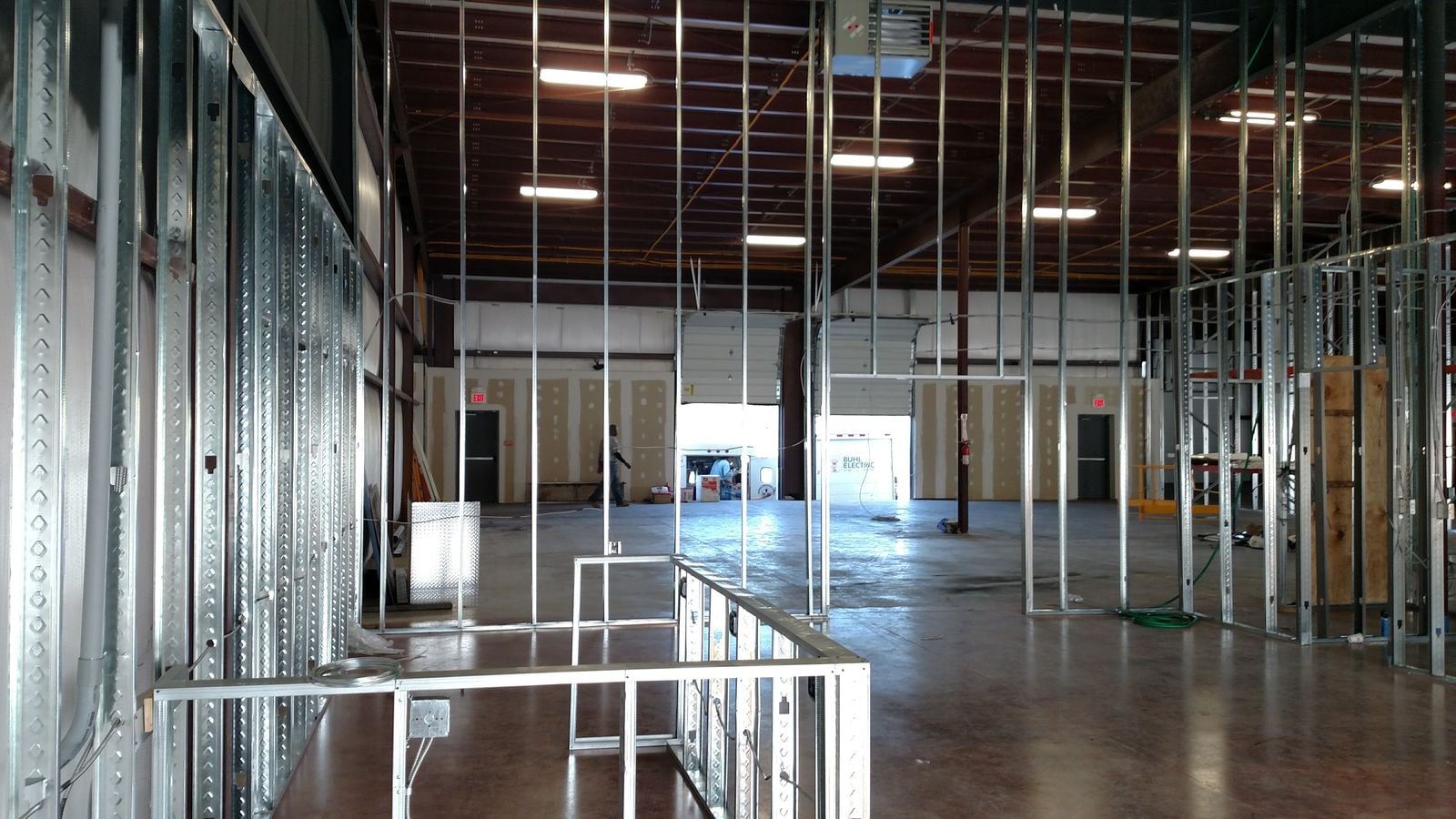 Steel stud framing across a large commercial interior with bay doors in the background